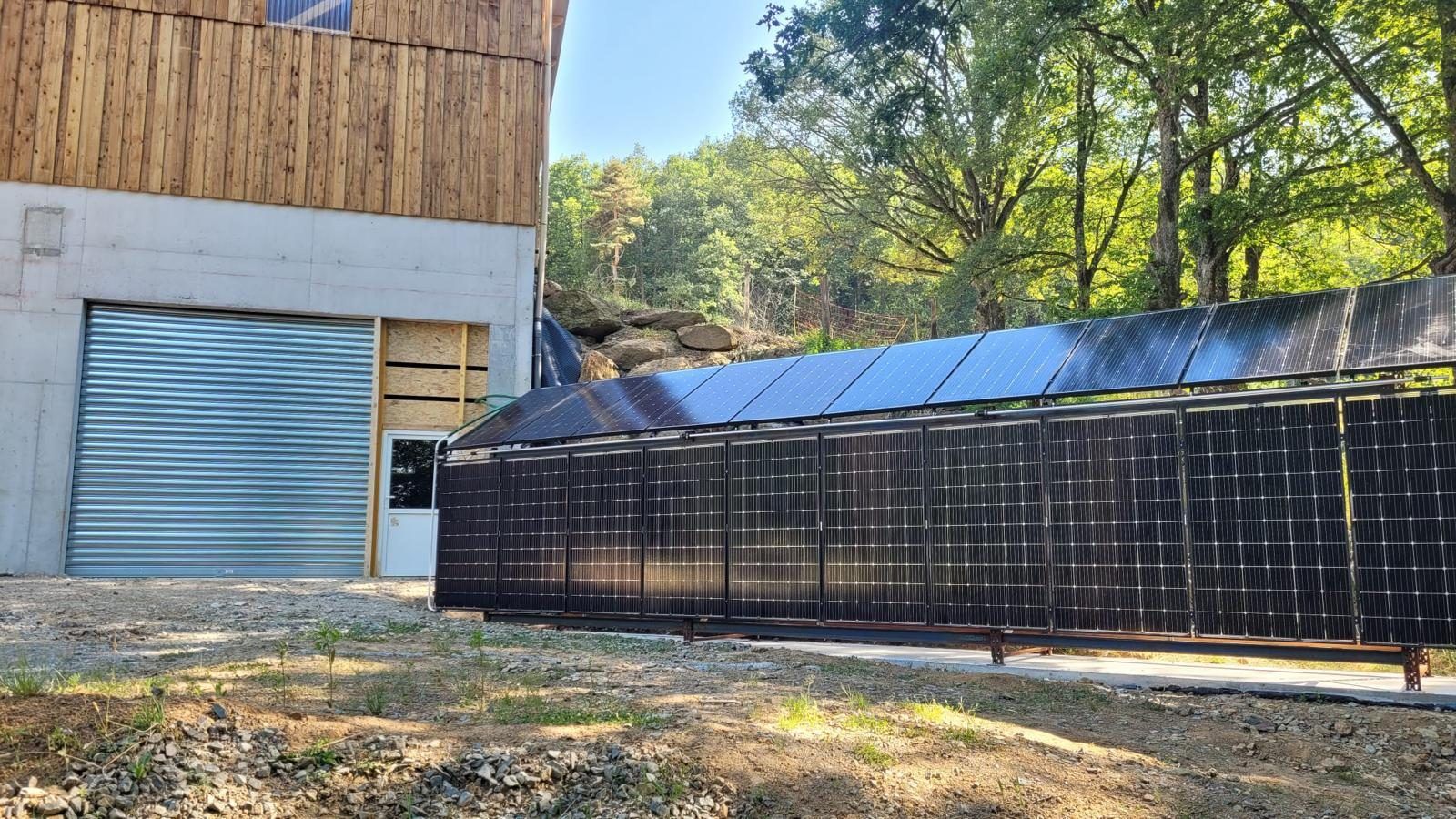 Double rangée de panneaux solaires installée au sol le long d'un bâtiment de séchage à bardage bois