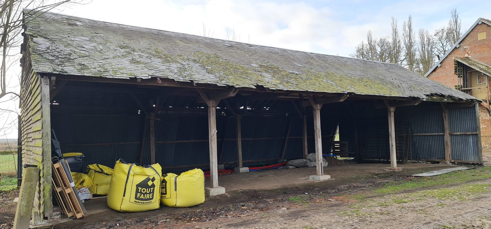 Hangar agricole existant en charpente bois avant installation du séchoir solaire, big-bags de matériaux et gaines posées au sol
