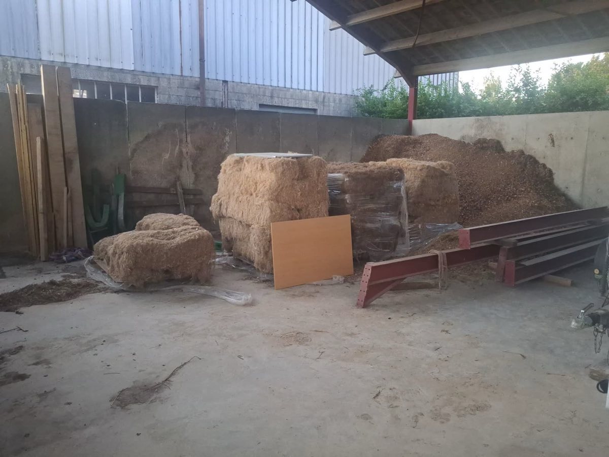 Balles de fibre végétale et tas de plaquettes de bois stockés au sec sous un hangar de séchage